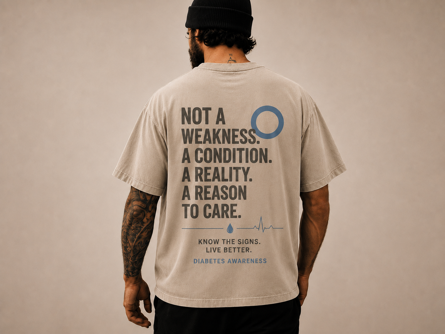 Rückenansicht eines sandfarbenen Oversize-Shirts mit dem Diabetes-Awareness-Print „Not a weakness. A condition. A reality. A reason to care.“ und blauem Kreis-Symbol